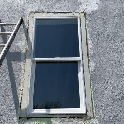 gray stucco wall with cracks with white window and trim partially removed